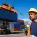 Trabalhador portuário acompanha o transporte de contêineres, representando a entrada em vigor da tarifa adicional dos EUA sobre produtos brasileiros.