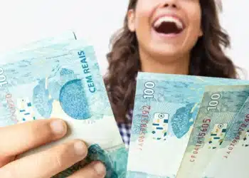 Mulher segura notas de real, representando o pagamento do terceiro lote da restituição do Imposto de Renda a 2,7 milhões de contribuintes.