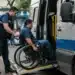 Eleitor com deficiência física em cadeira de rodas recebendo auxílio para embarcar em van adaptada, representando a ação de transporte para votação nas eleições de 2026.