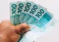 Pessoa segurando cédulas de real, representando o pagamento do último lote da restituição do Imposto de Renda 2026.