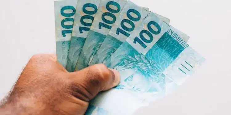 Pessoa segurando cédulas de real, representando o pagamento do último lote da restituição do Imposto de Renda 2026.