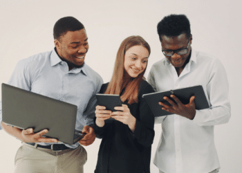Pessoas com formação em tecnólogo utilizando notebook e tablet em ambiente profissional, representando oportunidades em concursos públicos.
