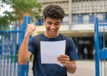 Estudante segurando documento de aprovação em frente a uma instituição de ensino, representando as vagas ofertadas pelo Fies 2026.2.