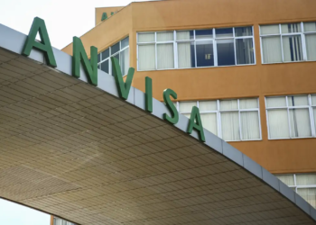 Letreiro verde ANVISA na entrada do prédio administrativo laranja com janelas em Brasília.