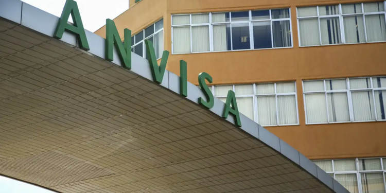 Letreiro verde ANVISA na entrada do prédio administrativo laranja com janelas em Brasília.