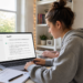 Jovem com cabelo preso e moletom cinza usa notebook com ChatGPT aberto em mesa de estudo clara