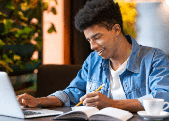 Jovem estudando com laptop e caderno em ambiente moderno.