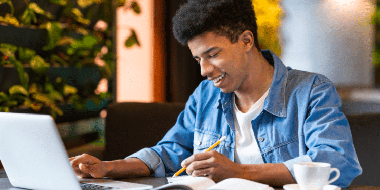 Jovem estudando com laptop e caderno em ambiente moderno.