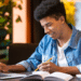 Jovem estudando com laptop e caderno em ambiente moderno.