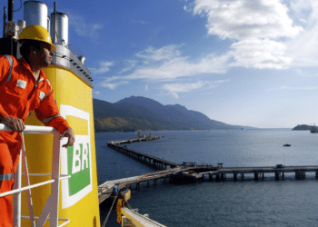 Trabalhador da Transpetro observa terminal marítimo com uniforme laranja.