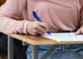 Estudante preenchendo prova em carteira escolar durante exame.