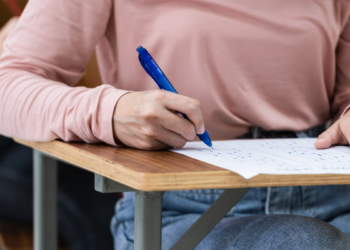 Estudante preenchendo prova em carteira escolar durante exame.