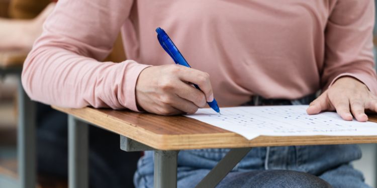 Estudante preenchendo prova em carteira escolar durante exame.