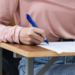 Estudante preenchendo prova em carteira escolar durante exame.
