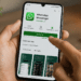 Mão masculina instala WhatsApp Messenger em smartphone com tela exibindo status instalando.