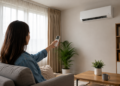 Mulher de cabelos longos liga ar-condicionado com controle remoto em sala decorada com plantas.