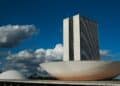 Prédio do Congresso Nacional com torres e cúpulas sob céu azul e nuvens em Brasília.