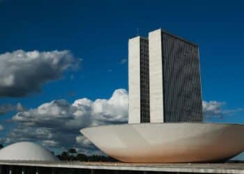 Prédio do Congresso Nacional com torres e cúpulas sob céu azul e nuvens em Brasília.