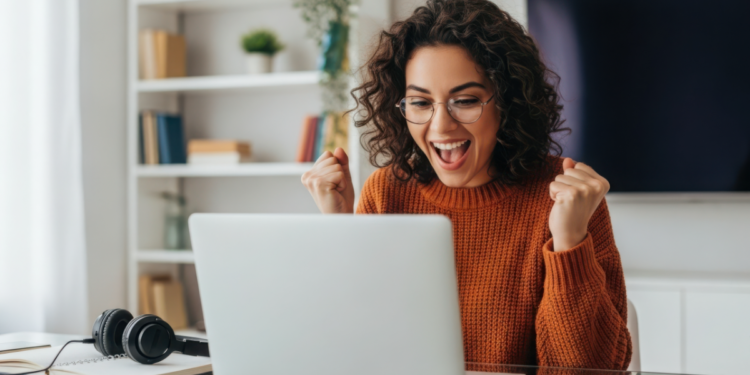 Jovem comemorando conquista ao computador ambiente doméstico alegre.
