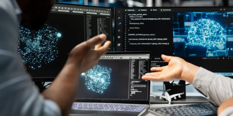 Profissionais analisam códigos e modelos de inteligência artificial em computadores durante desenvolvimento de soluções tecnológicas.