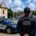 Dois guardas municipais de colete observam praça com viatura em frente à igreja colonial em Valença-BA.