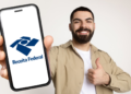 Jovem exibe aplicativo da Receita Federal em celular com expressão positiva.