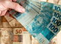 Notas de 100 e 50 reais sendo manuseadas em foco.