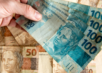Notas de 100 e 50 reais sendo manuseadas em foco.