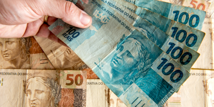 Notas de 100 e 50 reais sendo manuseadas em foco.