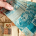 Notas de 100 e 50 reais sendo manuseadas em foco.