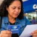 Mulher consulta cartão do PIS/Pasep e documento em frente a uma agência da Caixa