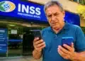 Homem idoso confere celulares em frente a uma agência do INSS, representando a manutenção do acesso ao Meu INSS após a troca de aparelho.