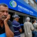 Homem aguarda atendimento diante de agência do INSS enquanto fila de beneficiários se estende pela calçada