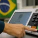 Mão de eleitor pressionando botão de confirmação em urna eletrônica durante votação no Brasil