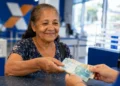Idosa recebe dinheiro em agência bancária, representando o pagamento dos benefícios do INSS de agosto.