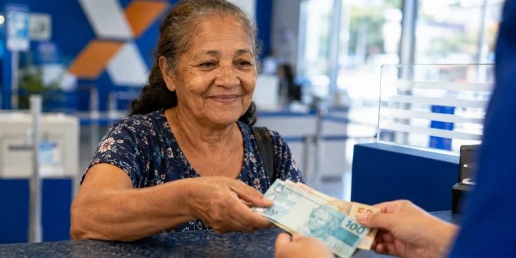 Idosa recebe dinheiro em agência bancária, representando o pagamento dos benefícios do INSS de agosto.