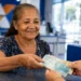 Idosa recebe dinheiro em agência bancária, representando o pagamento dos benefícios do INSS de agosto.