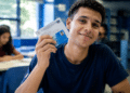 Estudante universitário segurando documento de identificação em sala de aula representando a Bolsa Permanência do Prouni.