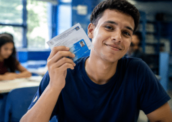 Estudante universitário segurando documento de identificação em sala de aula representando a Bolsa Permanência do Prouni.