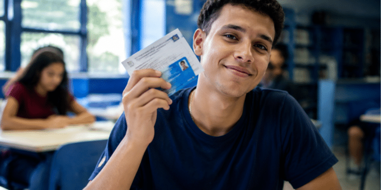 Estudante universitário segurando documento de identificação em sala de aula representando a Bolsa Permanência do Prouni.