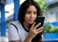 Estudante consulta informações do Pé-de-Meia pelo celular em ambiente escolar.