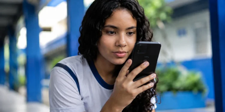 Estudante consulta informações do Pé-de-Meia pelo celular em ambiente escolar.