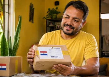 Homem segura encomenda com bandeira do Paraguai e etiqueta dos Correios dentro de casa.
