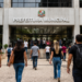 Pessoas caminhando em direção à entrada de uma Prefeitura Municipal durante seleção pública.