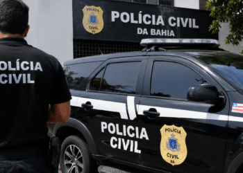 Viatura e agente da Polícia Civil da Bahia em frente à unidade policial.