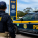 Policial Rodoviário Federal ao lado de viatura da PRF durante operação em rodovia.