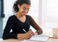 Pessoa estudando para concurso público com material de preparação sobre a mesa.
