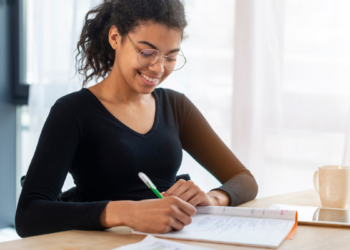 Pessoa estudando para concurso público com material de preparação sobre a mesa.