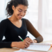 Pessoa estudando para concurso público com material de preparação sobre a mesa.