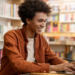 Estudante se prepara para concursos públicos usando notebook em biblioteca com livros ao fundo.